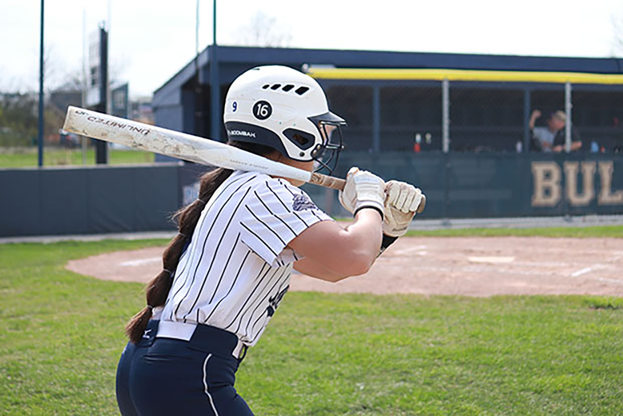 Softball player warms up with #16 displayed on her helmet.